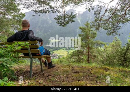 Europa, Austria, Tirolo, Alpi di Ötztal, Ötztal, escursionista si siede su una panchina con vista su Sautens e sulle montagne circostanti Foto Stock
