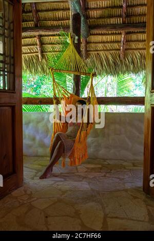 America, Caraibi, Greater Antilles, Repubblica Dominicana, Cabarete, donna seduta in un'amaca sulla terrazza del suo bungalow nel natura Cabana Boutique Hotel & Spa Foto Stock