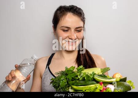 La ragazza tiene una bottiglia d'acqua e un piatto con verdure verdi nelle mani. Nutrizione adeguata, verdure nella dieta, dieta del keto, disintossicazione del corpo Foto Stock