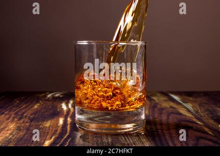 Il whisky viene versato in un bicchiere. Bevanda alcolica di alto livello Fiery in un bar su sfondo di legno scuro. Foto Stock