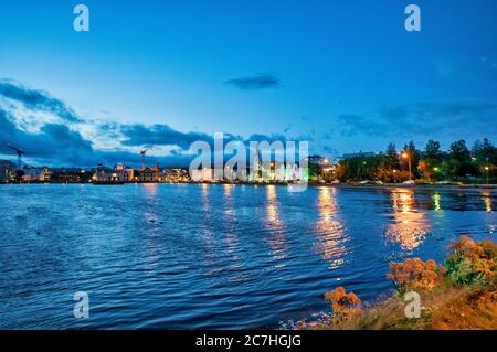 Belle case lungo il lago Tjornin di notte, Reykjavik, Islanda. Foto Stock