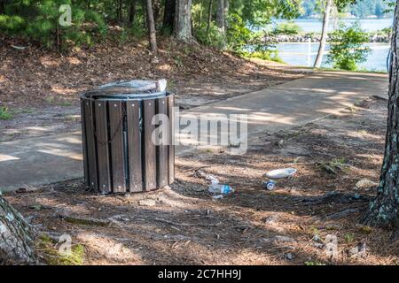 Lungo il sentiero con il lago sullo sfondo, possono essere posati sul terreno diversi pezzi di carta plastica e alluminio da un bidone traboccante Foto Stock