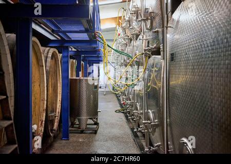 Vasche di rash in acciaio inox e grandi barili in legno nella cantina di fermentazione con tubi e tubi Foto Stock