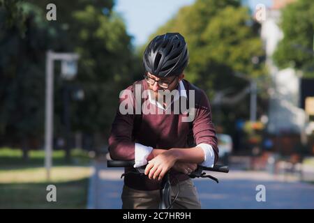 Ritratto di un pendolarista millenario in un casco da bicicletta. Ciclismo sicuro in città, andando a lavorare su una bicicletta, moderna immagine di stile di vita urbano Foto Stock