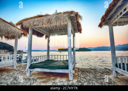 Tettoie e tende dal tetto di paglia sulla spiaggia Copacabana al tramonto a Dubrovnik. Ubicazione: Dubrovnik, Dalmazia, Croazia, Europa Foto Stock