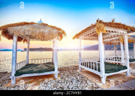 Tettoie e tende dal tetto di paglia sulla spiaggia Copacabana al tramonto a Dubrovnik. Ubicazione: Dubrovnik, Dalmazia, Croazia, Europa Foto Stock