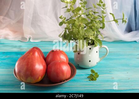 Pomodori rosa di paese maturi su un tavolo di legno blu. Nella tazza - un mazzo di Melissa Foto Stock