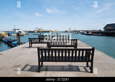 Panchine di legno nel Royal Harbour, Ramsgate, che si affaccia verso il faro e una fine del ristorante molo Foto Stock