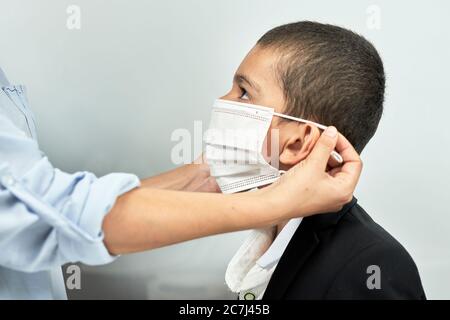 Ritorno a scuola. Madre che prepara il figlio a scuola. Scolaro pronto ad andare a scuola. La mamma mette la maschera di sicurezza Foto Stock