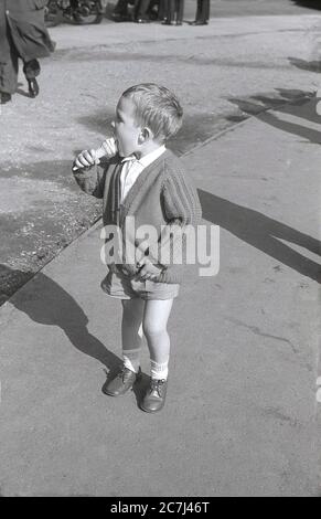 Anni '60, storico, in estate e un ragazzo in pantaloncini e indossando un cardigan, mangiando un cono gelato in piedi su un percorso a Trafalgar Square, Londra, Inghilterra, Regno Unito. Foto Stock