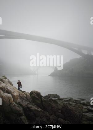 Porto, Portogallo - 25 aprile 2006: Uomo solo sulla riva del fiume Douro, vedendo due dei famosi e bei ponti di Porto nella nebbia mattutina. Foto Stock