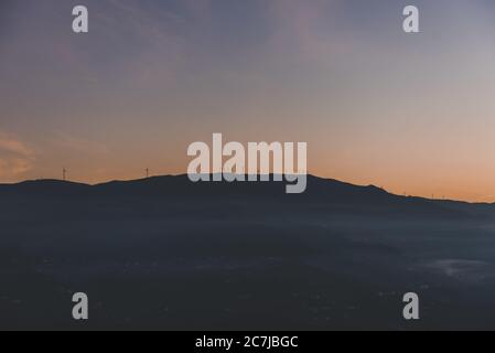 Silhouette di una montagna con mulini a vento sulla cima Foto Stock