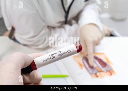 Provetta per analisi del sangue per virus corona positivo, e medico femminile con maschera stanca in background Foto Stock