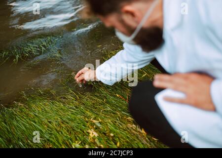 Biologo e ricercatore di scienziato caucasico maschile in tuta protettiva con maschera che preleva campioni d'acqua dal fiume inquinato. Foto Stock