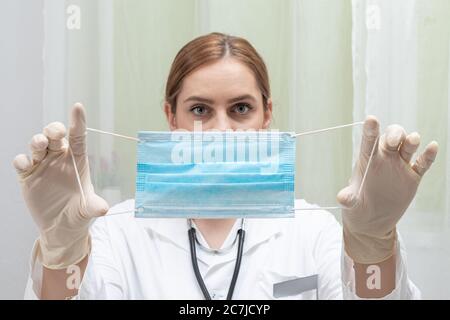 dottore femminile che mette la maschera medica sul viso in ufficio medici Foto Stock