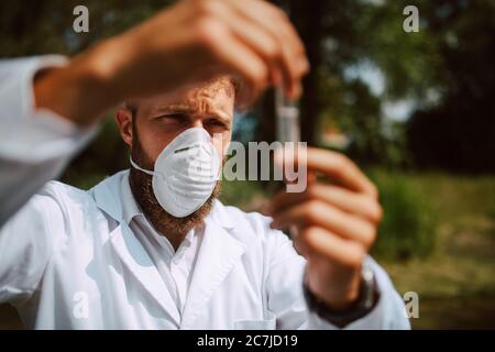 Biologo e ricercatore di scienziato caucasico maschile in tuta protettiva con maschera che preleva campioni d'acqua dal fiume inquinato. Foto Stock