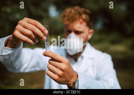 Biologo e ricercatore di scienziato caucasico maschile in tuta protettiva con maschera che preleva campioni d'acqua dal fiume inquinato. Foto Stock