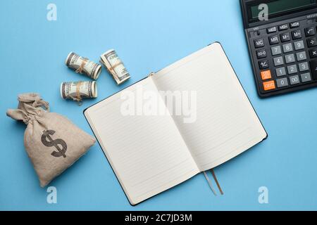 Una calcolatrice, un diario accanto a un sacco di soldi su sfondo blu Foto Stock