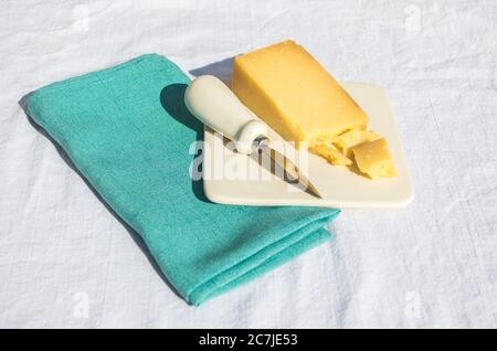 un cuneo di formaggio cheddar su un piatto di formaggio con un piccolo coltello su un tovagliolo di lino verde in un picnic Foto Stock