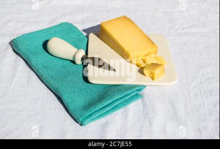 un cuneo di formaggio cheddar su un piatto di formaggio con un piccolo coltello su un tovagliolo di lino verde in un picnic Foto Stock