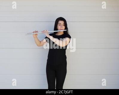 La ragazza dai capelli neri gioca il flauto all'esterno davanti a uno sfondo bianco Foto Stock