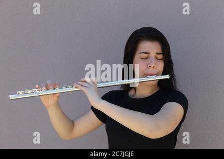 La ragazza dai capelli neri gioca il flauto all'esterno di fronte a un primo piano di sfondo grigio Foto Stock