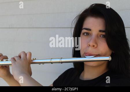 La ragazza dai capelli neri gioca il flauto all'esterno davanti a un primo piano di sfondo bianco Foto Stock