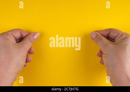 Mani con dita aggrinzite in un pizzico su sfondo giallo Foto Stock