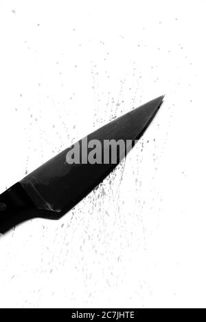 Immagine verticale in scala di grigi di un coltello nero e di alcuni sangue spruzzato su una superficie bianca Foto Stock