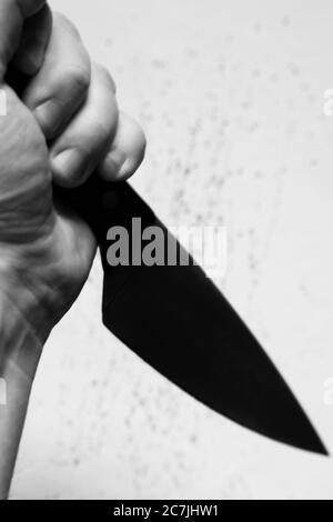 Immagine verticale in scala di grigi di una persona che tiene un nero coltello con sfondo bianco sfocato Foto Stock