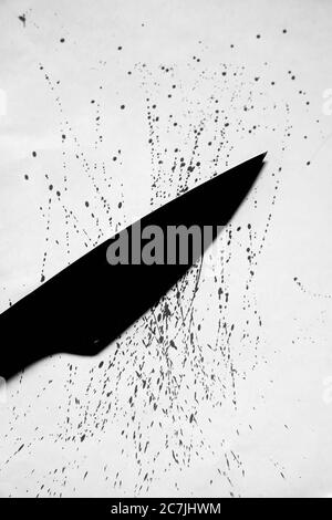 Immagine verticale in scala di grigi di un coltello nero con gocce di sangue spruzzato su una superficie bianca Foto Stock