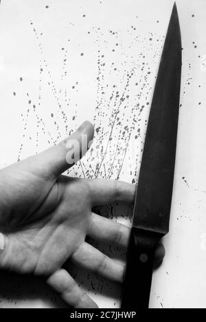 Immagine verticale in scala di grigi di una persona che tiene un coltello con gocce di sangue su una superficie bianca Foto Stock