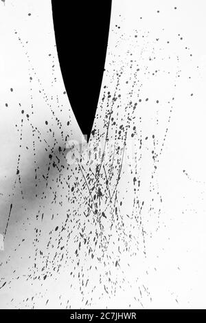 Immagine verticale in scala di grigi di un coltello nero e gocce di sangue spruzzato su una superficie bianca Foto Stock