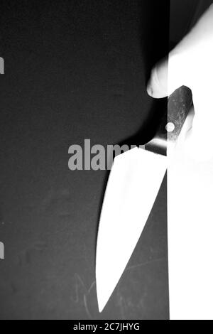 Immagine verticale in scala di grigi di una persona che tiene un coltello su una superficie nera Foto Stock