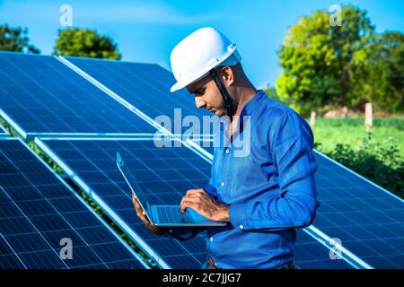 Giovane ingegnere maschile che lavora su un computer portatile in piedi vicino a pannelli solari, terra agricola con cielo azzurro chiaro sfondo, energia rinnovabile, energia pulita Foto Stock