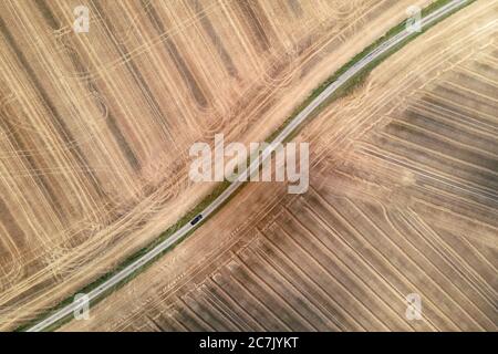 auto che guida su una piccola strada rurale circondata da campi raccolti, vista aerea drone Foto Stock