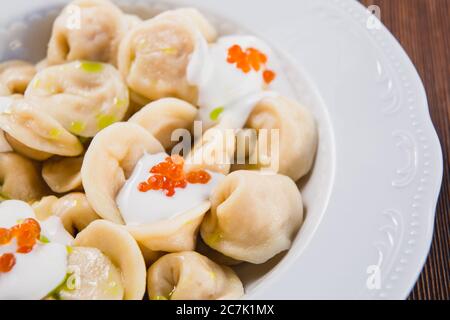 Ciotola con caviale rosso e panna acida su un tavolo marrone sullo sfondo del ristorante Foto Stock