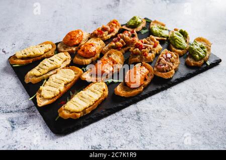 Bruschetta assortita con vari condimenti su un piatto scuro su sfondo bianco. Bruschetta appetitosa. Foto Stock