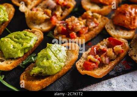 Bruschetta assortita con vari condimenti su un piatto scuro su sfondo bianco. Bruschetta appetitosa. Foto Stock