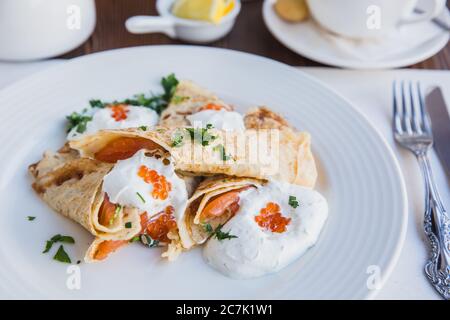 Piatto bianco con pancake con salmone e caviale rosso, servito con panna acida per colazione Foto Stock