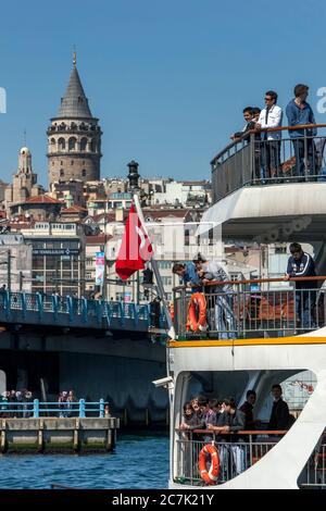 I passeggeri a bordo di un traghetto partono dal porto del Corno d'Oro nel quartiere Eminonu di Istanbul, in Turchia. Sullo sfondo si trova la Torre Galata. Foto Stock