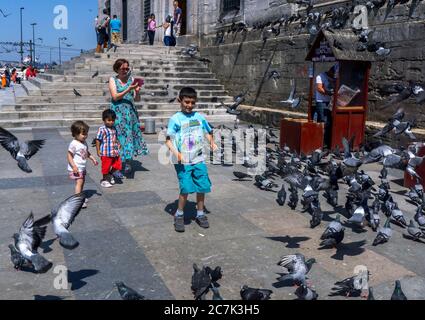 I bambini cercano di catturare i piccioni riuniti accanto al 400 anni Yeni Camii nel distretto Eminonu di Istanbul in Turchia. Foto Stock