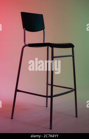 Una sedia alta si trova in uno studio fotografico su uno sfondo di carta bianca illuminato in toni rosso-verde Foto Stock