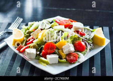 Insalata di verdure sul piatto, pomodori, insalata verde, formaggio, limone e olive, altre verdure. Su fondo nero. Foto Stock