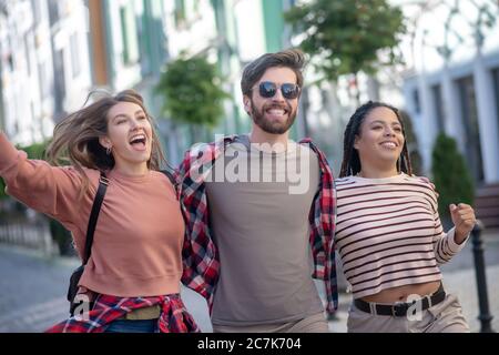 Ragazzo in occhiali da sole e due ragazze graziose che camminano entusiaste Foto Stock