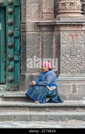 Cusco, Perù - 22 ottobre 2008: Donna in tradizionale conca seduta di fronte alla Cattedrale delle porte ornate di legno verde della Cattedrale di Santo Domingo Foto Stock