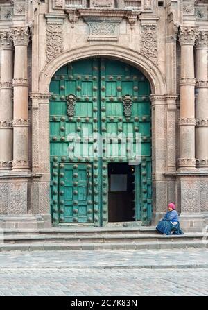 Cusco, Perù - 22 ottobre 2008: Donna in tradizionale conca seduta di fronte alla Cattedrale delle porte ornate di legno verde della Cattedrale di Santo Domingo Foto Stock
