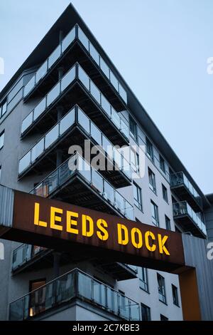 LEEDS, REGNO UNITO - 11 gennaio 2020: Scatto verticale di un cartello del molo di Leeds si è acceso su su su una notte nuvolosa del crepuscolo con un blocco di appartamenti dietro Foto Stock