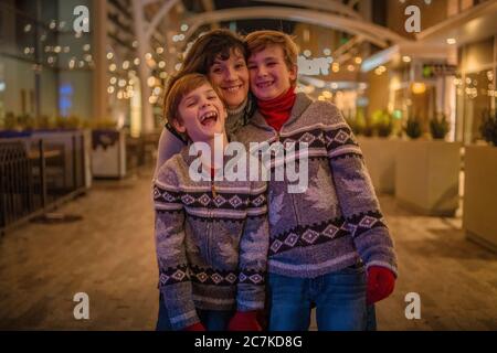 Madre con i suoi due figli in giacche identiche che si posano all'esterno - concetto di tempo familiare Foto Stock