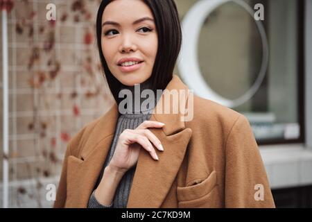 Ritratto di bella ragazza asiatica in cappotto che guarda fuori in modo sognante Foto Stock